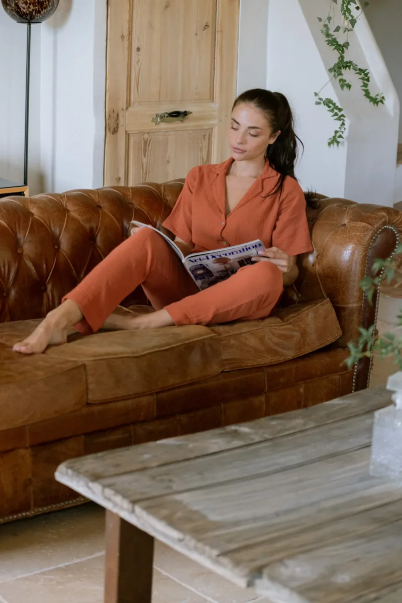 Pantalon de pyjama Daphné terracotta en gaze de coton bio, porté sur un canapé